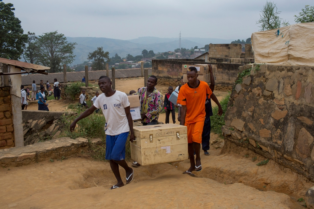 Twee mannen dragen een grote koelbox waarin de vaccines tegen gele koorts zitten. Medewerkers van AZG vernevelen een wijk in Matadi om er de muggen uit te roeien. © MSF