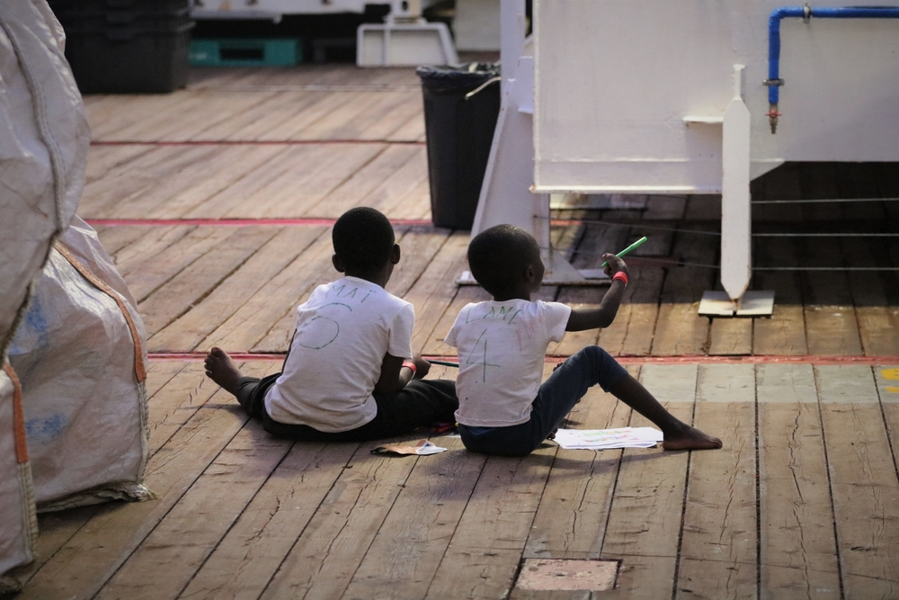 Twee geredde kinderen aan boord van het schip maken samen een tekening. ©