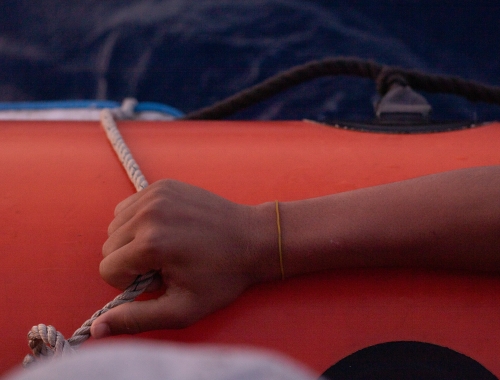 Une main tient la corde sur un canot de sauvetage rouge.